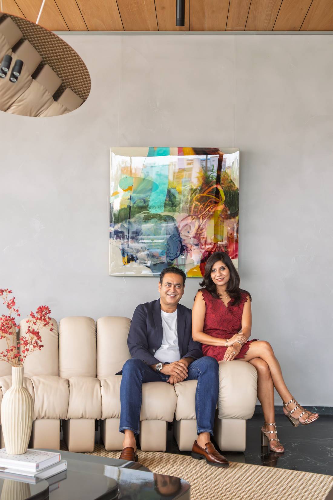 Prachi and Avinash Agarwal seated on an ivory modular sofa beneath a large abstract artwork